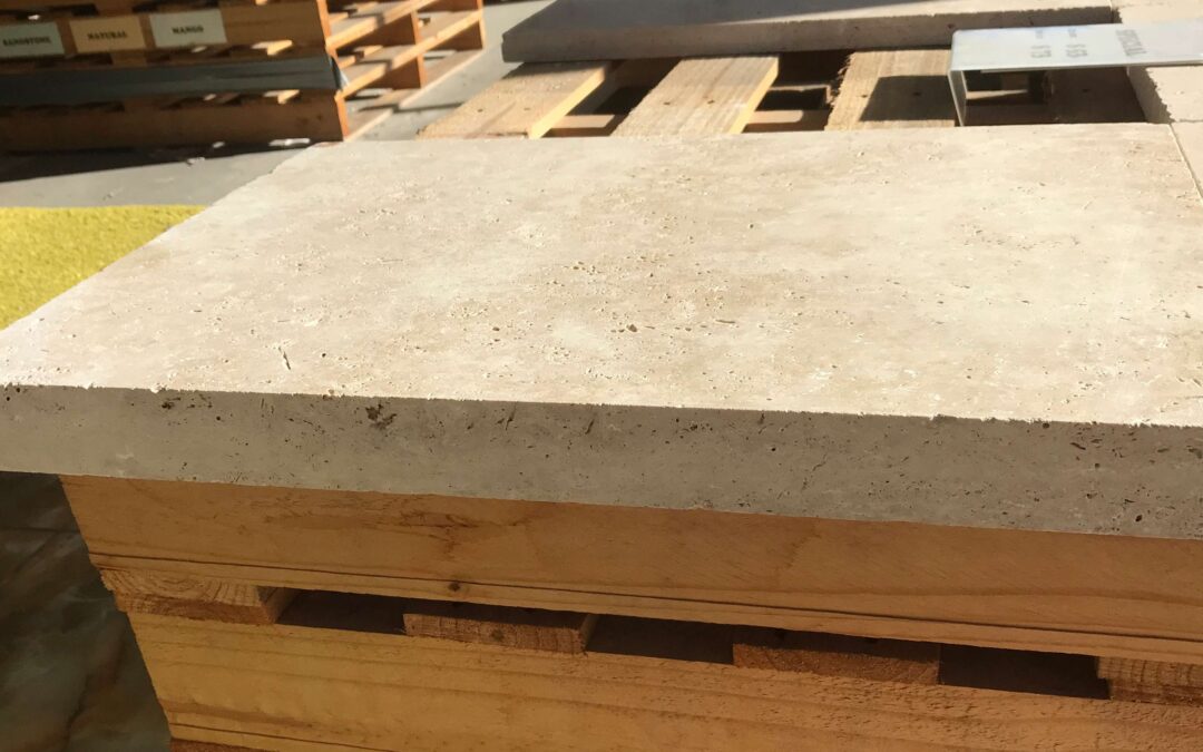 Beige natural travertine drop face pool coping tile resting on a timber pallet in a Melbourne stone yard warehouse