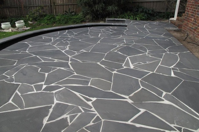 Dark charcoal bluestone crazy paving patio with light-coloured mortar joints in a Melbourne residential backyard garden